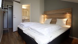 A bedroom with a bed, a wooden headboard, a wardrobe, and a bathroom visible through an open door. - Kvibergs Vandrarhem - Hostel (Gothenburg)