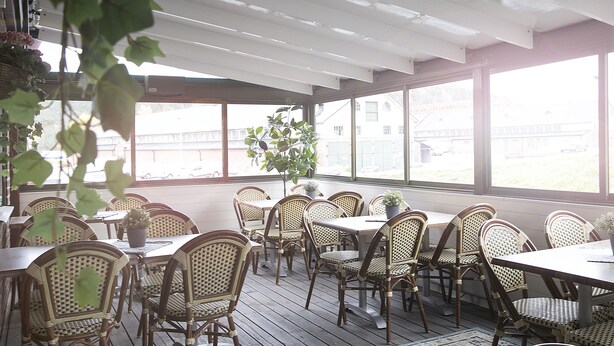 An outdoor patio with wicker tables and chairs, large windows, and potted plants. - Kvibergs Vandrarhem - Hostel (Gothenburg)