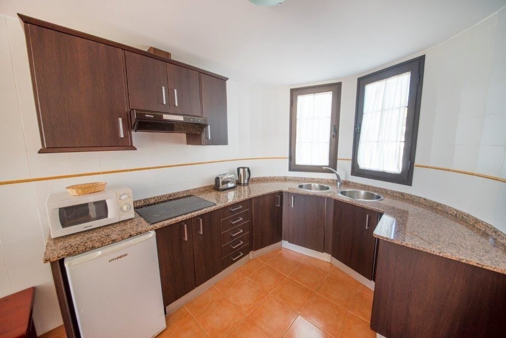 Una cocina compacta con armarios de madera oscura, un microondas, un tostador y un lavabo.