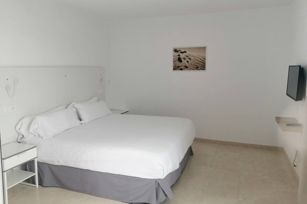 A bedroom with a bed, a bedside table, a wall-mounted TV, and a small picture on the wall.