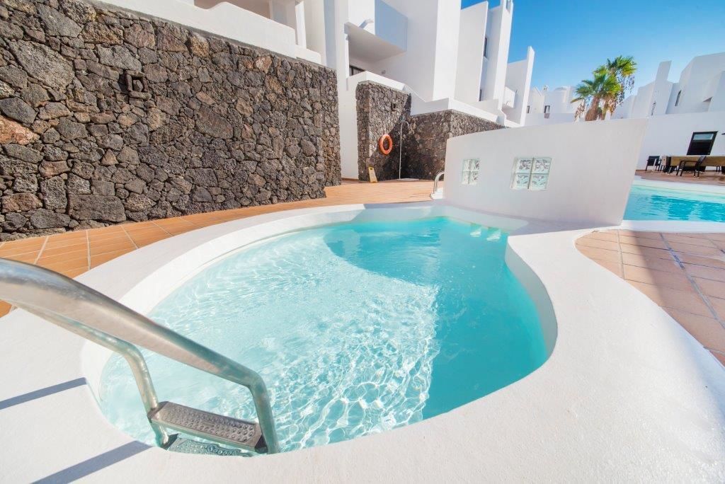 Una piscina con un muro de piedra y un edificio blanco al fondo.