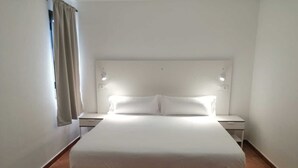 A hotel room with a large bed, two bedside tables, and a window with curtains. - Tabaiba Apartamentos (Teguise)