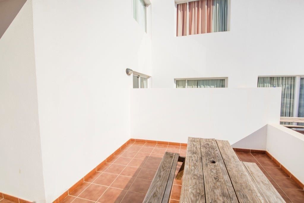 A small, enclosed balcony with a wooden table and tiled flooring.