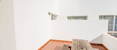 A small, enclosed balcony with a wooden table and tiled flooring.