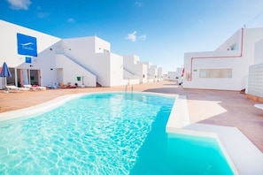 A pool area with white buildings, a blue sign, and a clear sky. - Tabaiba Apartamentos (Teguise)