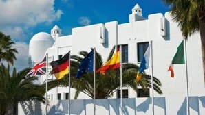 A white building with a dome and multiple flags, including the UK, Germany, EU, and Italy, indicating a location of international significance. - Tabaiba Apartamentos (Teguise)