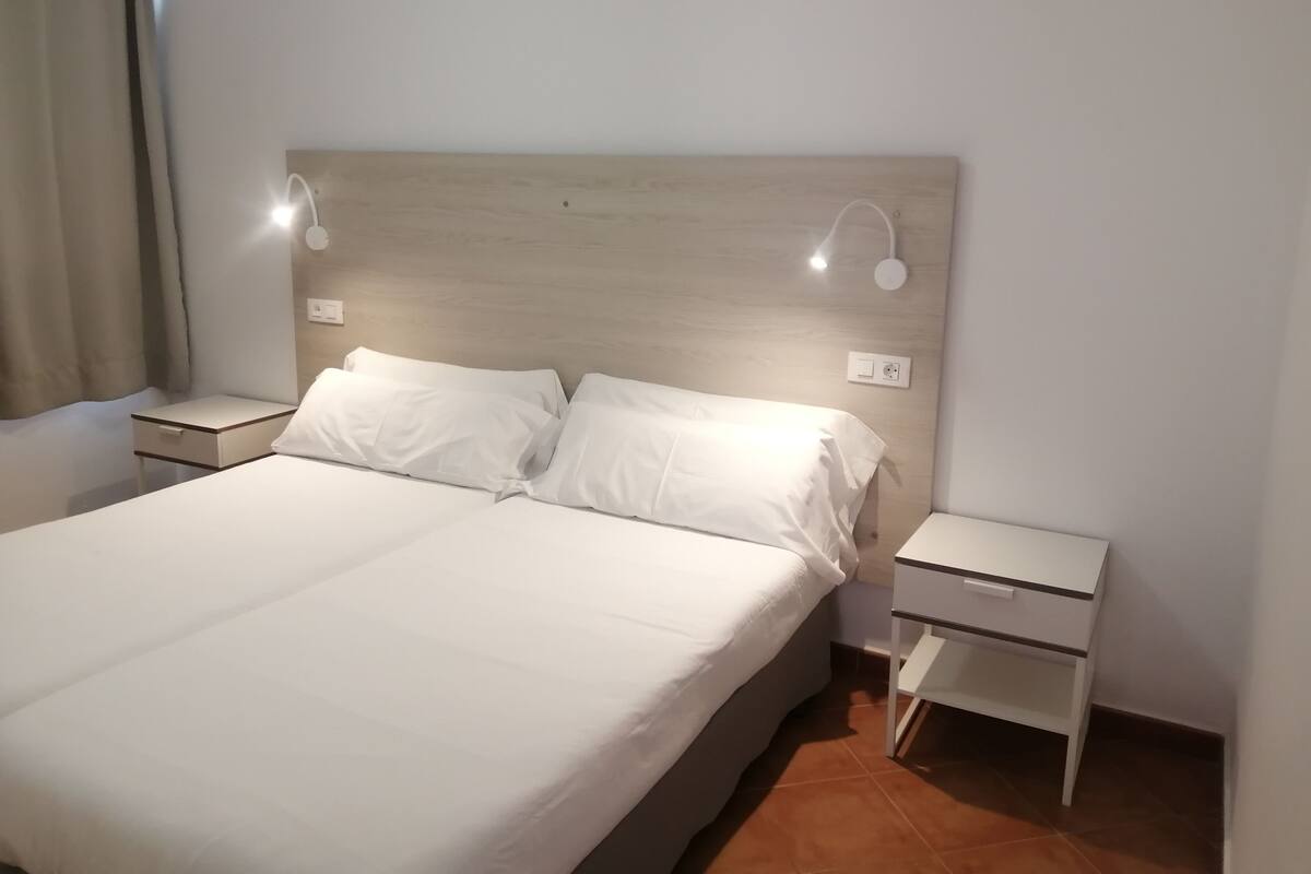 A neatly made bed with white linens, two bedside tables with lamps, and a light-colored headboard.