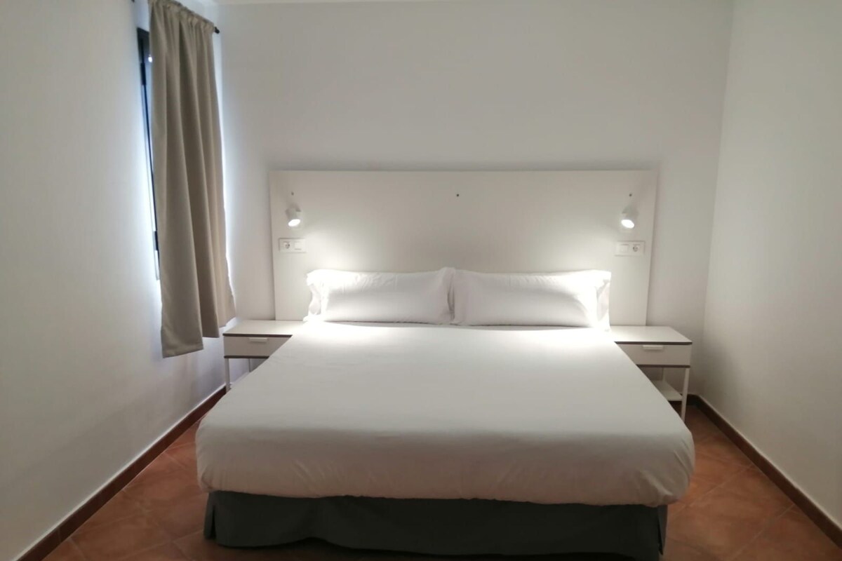 A hotel room with a large bed, two bedside tables, and a window with curtains.