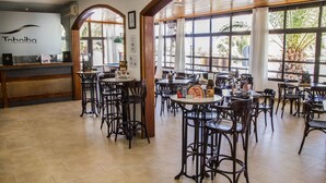 A restaurant interior with high wooden beams, large windows, and multiple tables and chairs. - Tabaiba Apartamentos (Teguise)