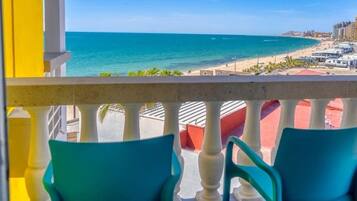 A balcony with turquoise chairs, a view of the beach, and a clear blue sky.