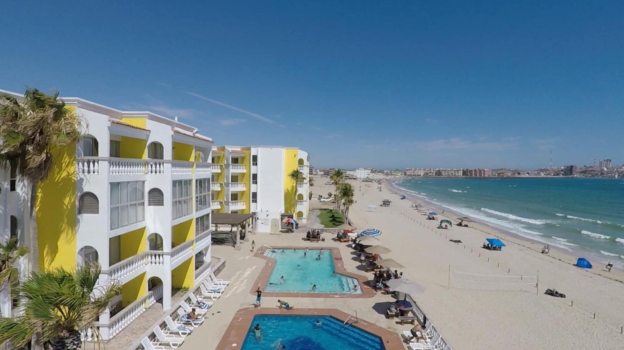 Un hôtel doté de plusieurs piscines, d’une plage et offrant une vue sur le paysage urbain en arrière-plan.