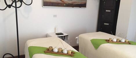 Quarto com duas camas, um quadro na parede, uma mesinha com uma garrafa e uma planta.