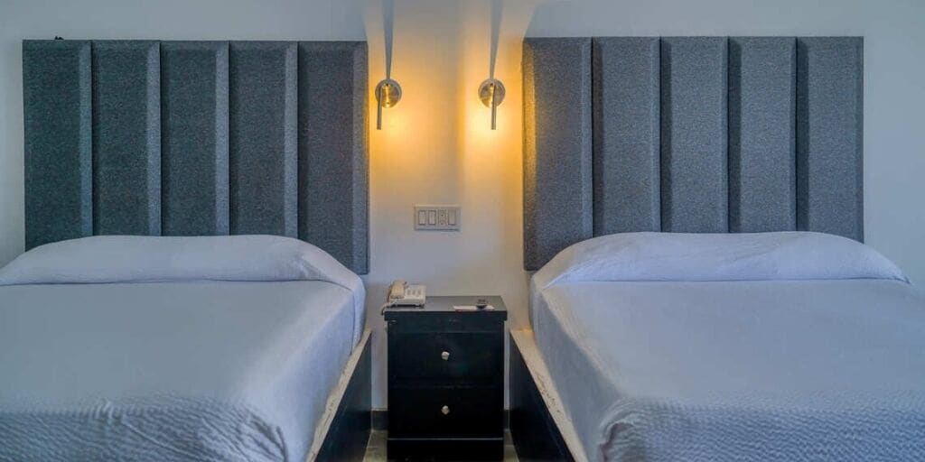 Habitación de hotel con dos camas individuales, una mesita de noche con teléfono y dos luces fijadas a la pared.
