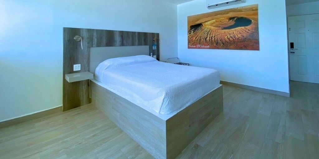 A single bed in a room with a wooden headboard, a painting on the wall, and a door in the background.