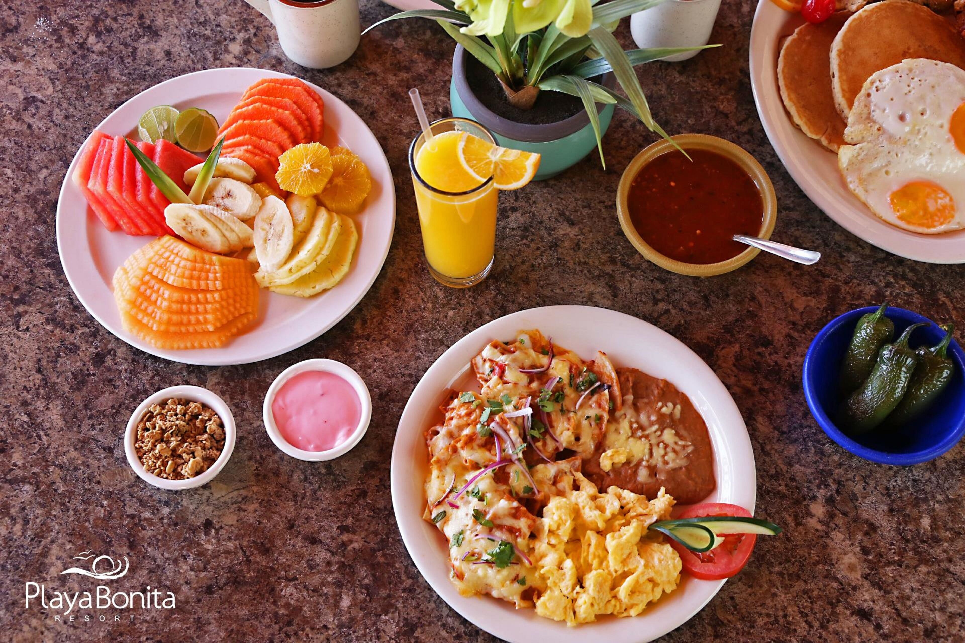 A breakfast spread with various dishes and drinks on a granite countertop.