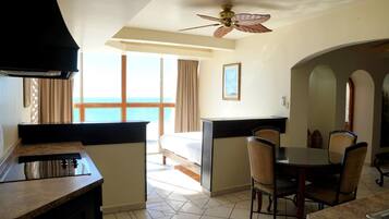 A room with a kitchen area, dining table, chairs, and a view of the ocean.