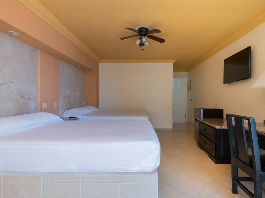 A hotel room with two beds, a ceiling fan, a television mounted on the wall, and a desk with a chair.