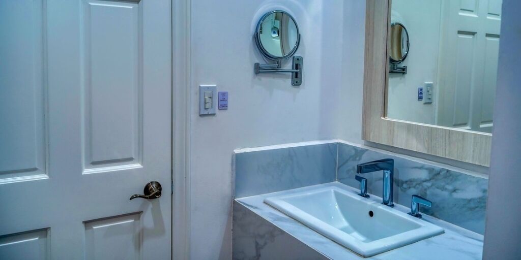 Een badkamer met een witte deur, een wastafel met een marmeren blad en een spiegel boven de wastafel.