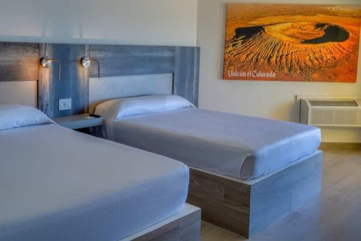Une chambre d’hôtel avec deux lits, une tête de lit en bois et un tableau représentant un volcan.