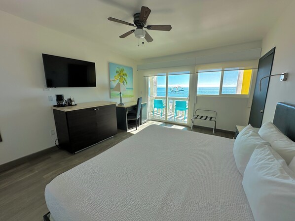 A hotel room with a bed, a desk, a chair, a TV, a ceiling fan, and a balcony with a view of the ocean. - Playa Bonita (Puerto Peñasco)