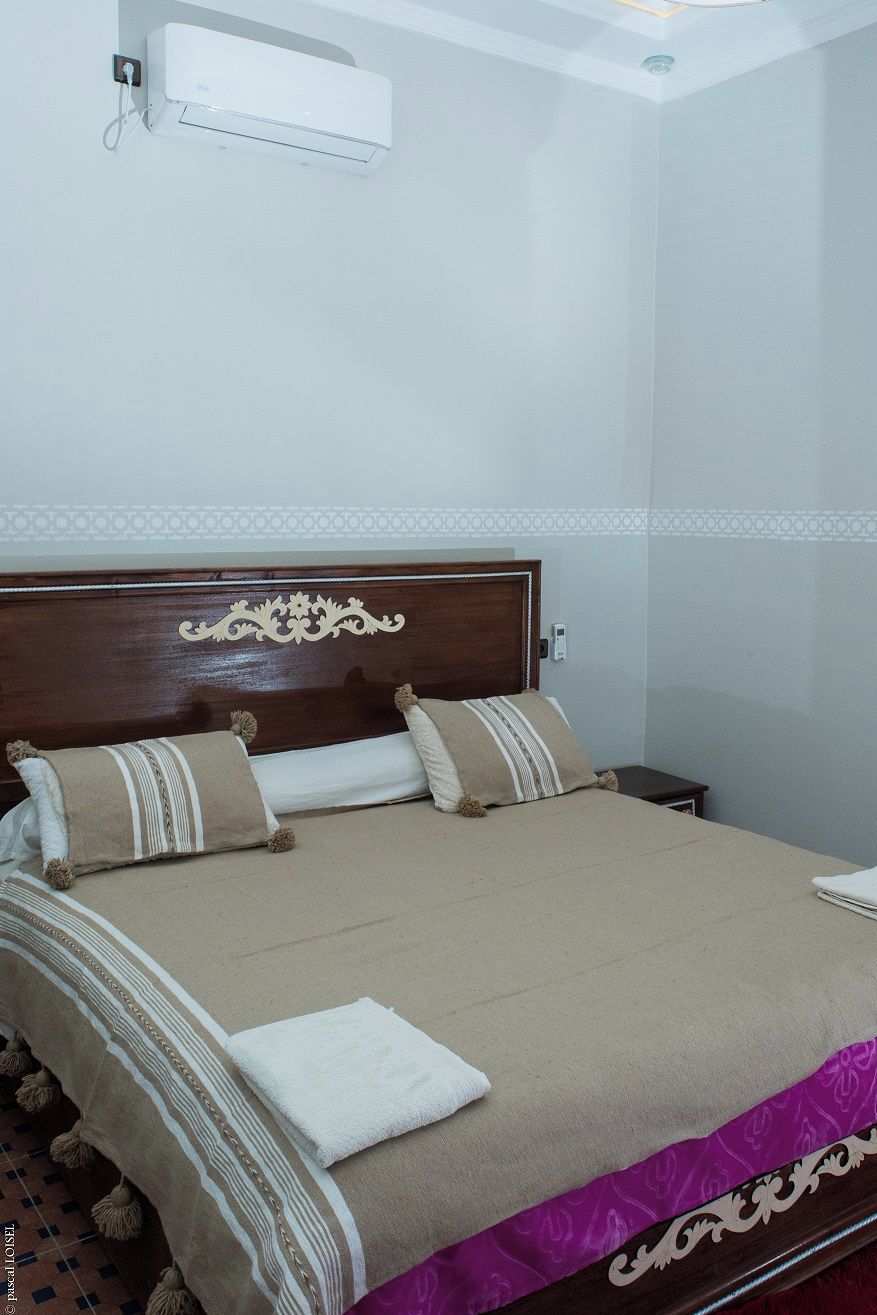 A hotel room with a bed, a nightstand, and a wall-mounted air conditioner.