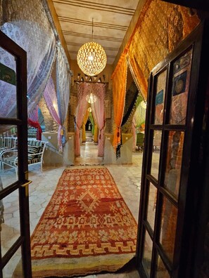 Un pasillo con alfombra estampada, un candelabro y telas drapeadas en las paredes.