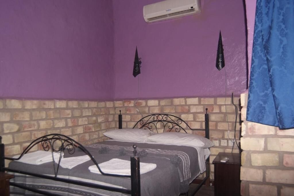 Une pièce avec un lit adossé à un mur de briques, une fenêtre avec un rideau bleu et un appareil de climatisation fixé au mur.