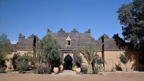 A traditional building with a central archway, surrounded by potted plants and palm trees.