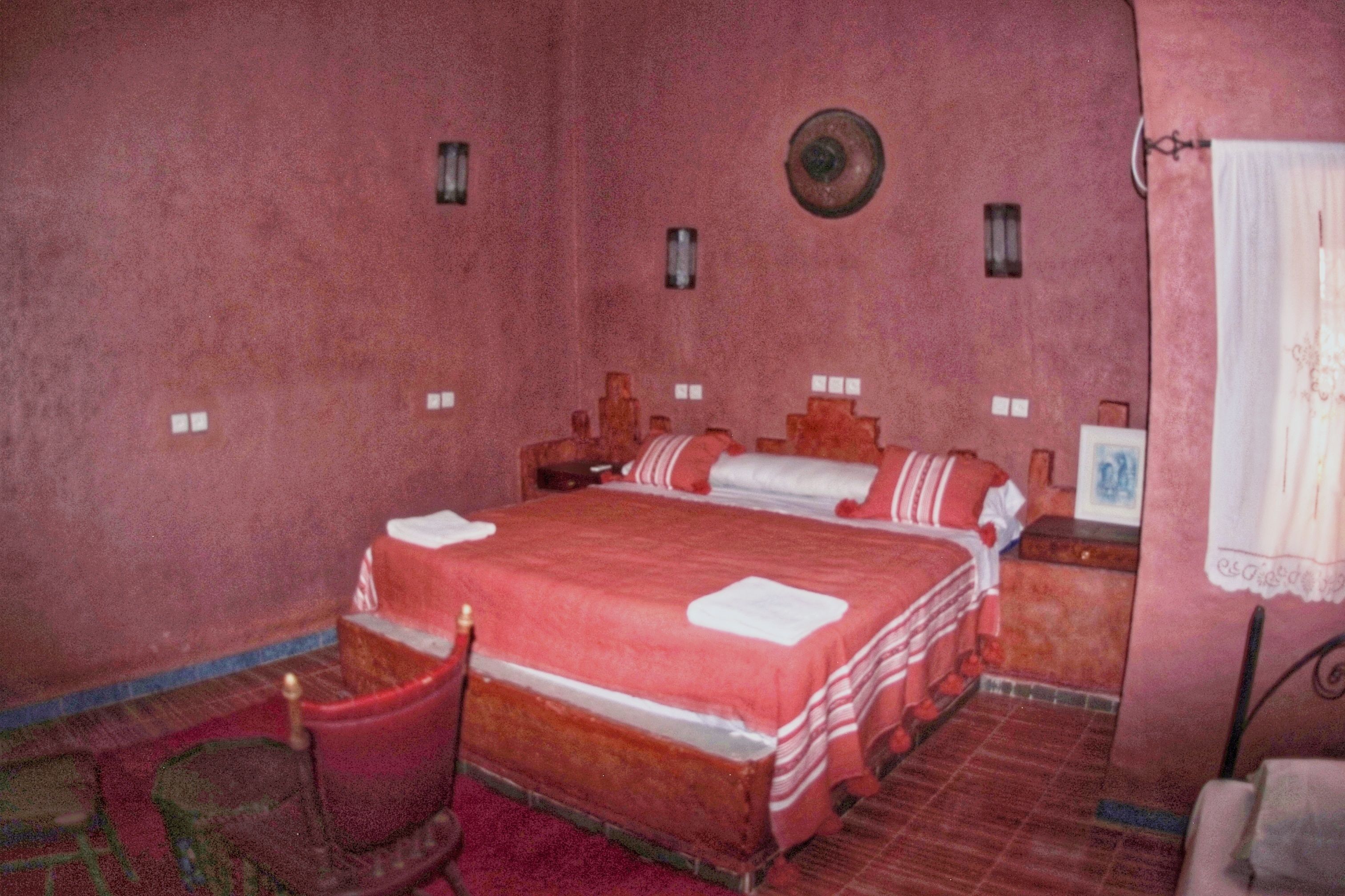 Un dormitorio con una cama grande, una mesita de noche de madera, una silla y una pequeña mesa con lámpara.