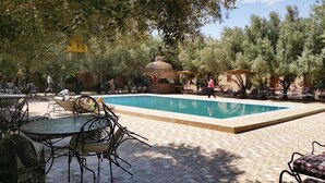 A swimming pool with tiled flooring, surrounded by outdoor seating and trees.