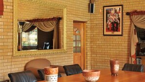 A dining area with a wooden table, black chairs, a brick wall, a framed mirror, and a painting. - Hoyohoyo Chartwell Lodge (Chartwell)