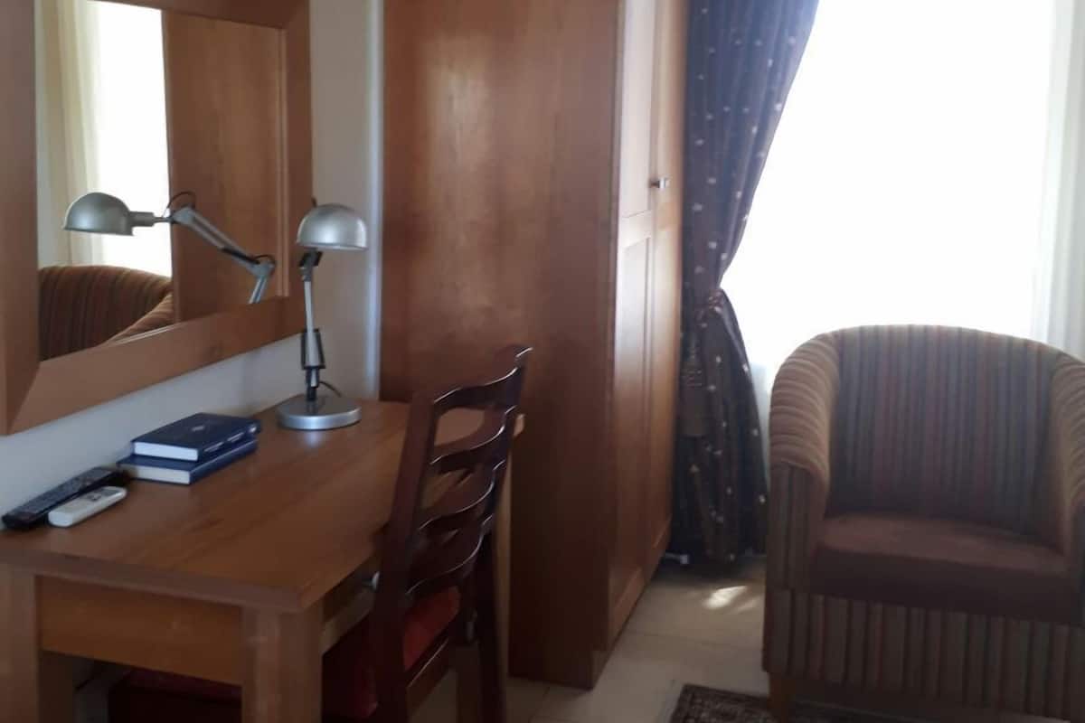 Habitación de hotel con escritorio de madera, una silla, televisor montado en la pared y ventana con cortinas.