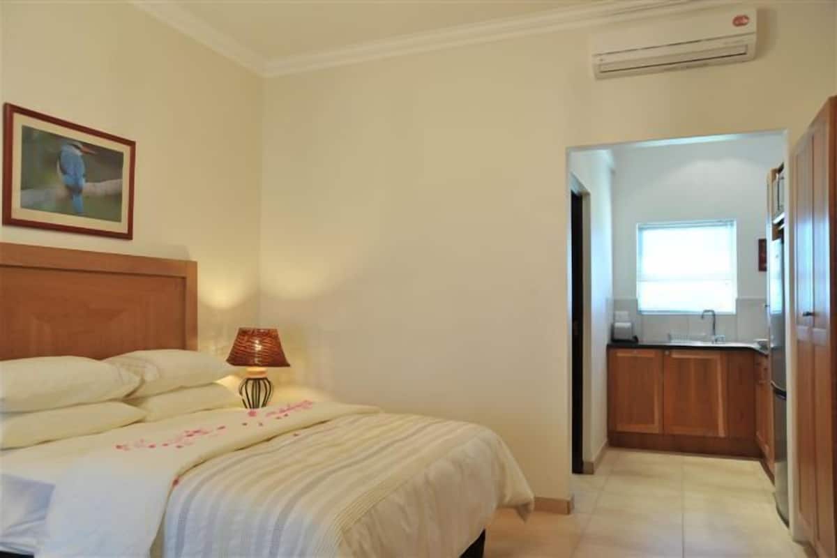 Un dormitorio con cama, mesita de noche, lámpara y un cuadro en la pared.