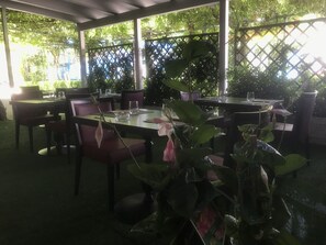 An outdoor dining area with tables and chairs, surrounded by greenery and a lattice fence. - Albergo Ristorante Protti (Cattolica)