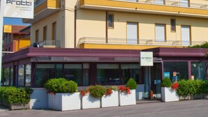 Un restaurant anomenat Protti amb una façana moderna, grans finestres i jardineres florals al llarg del passeig.