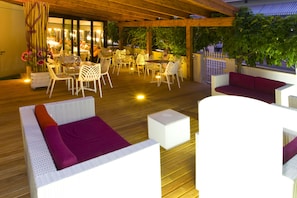 An outdoor patio with white wicker furniture, including sofas and chairs, and a wooden deck. - Albergo Ristorante Protti (Cattolica)