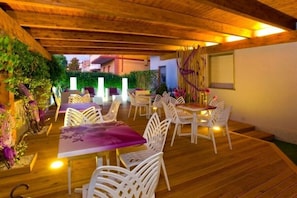 An outdoor patio with wooden flooring, white plastic chairs, and tables. - Albergo Ristorante Protti (Cattolica)