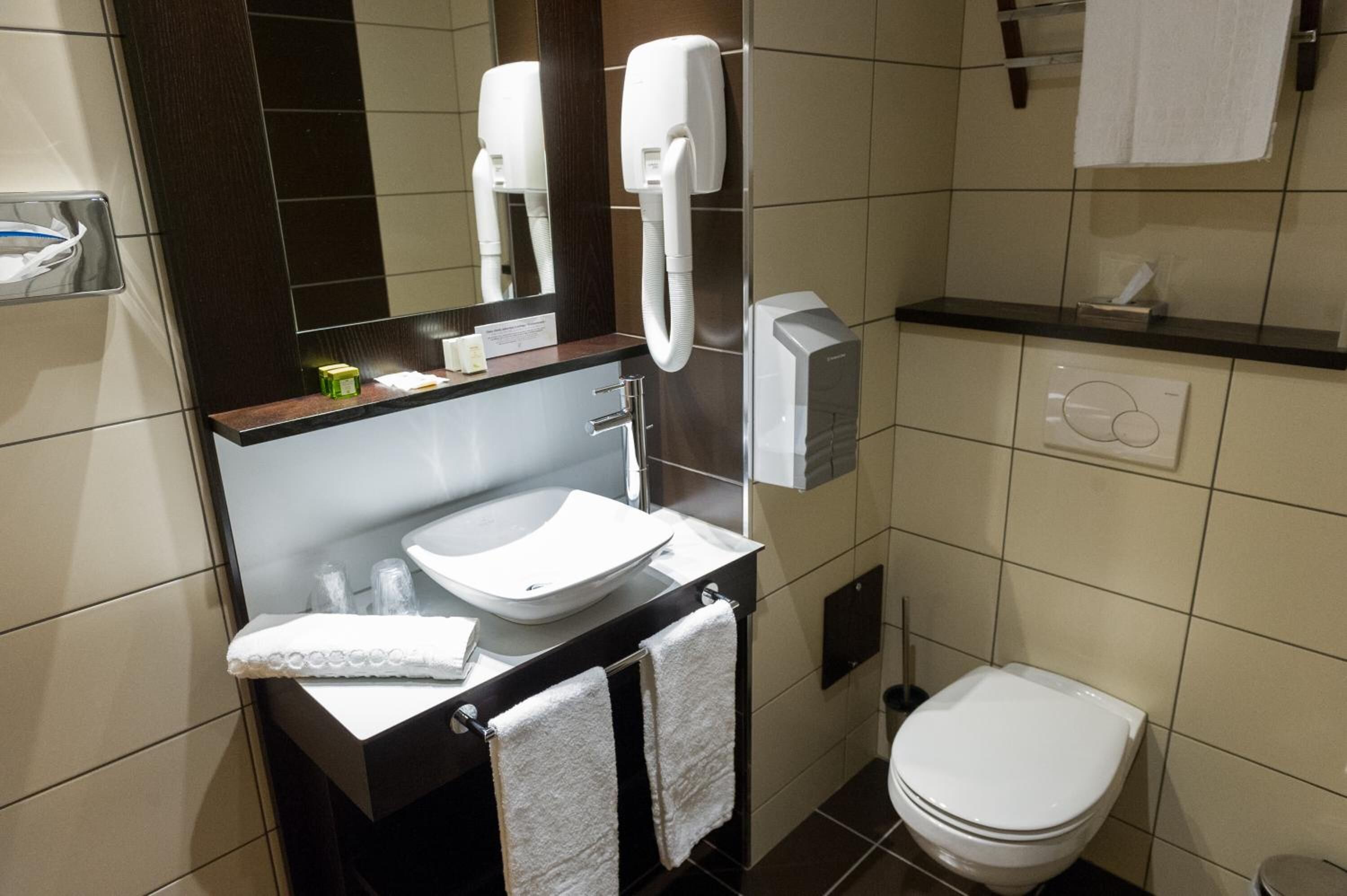 Et moderne badeværelse med vask, spejl, håndklædestige og toilet.