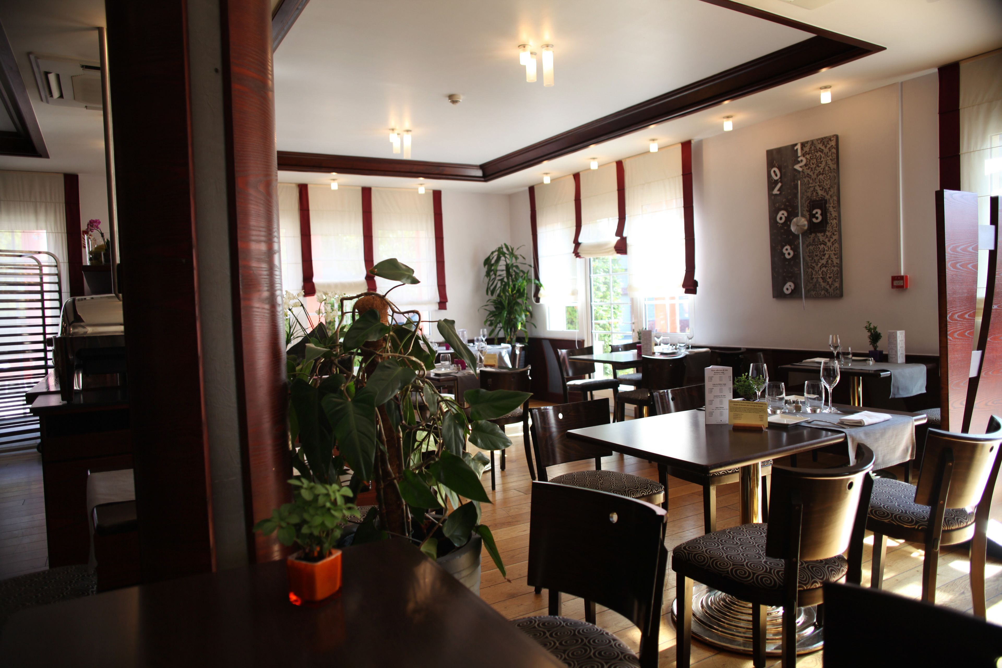 Un vaste espace dédié à la salle à manger, avec des tables et des chaises en bois, des plantes en pot et une grande horloge murale.
