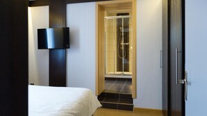 Una habitación de hotel moderna con una cama, un televisor montado en la pared y una zona de ducha con puertas de cristal.