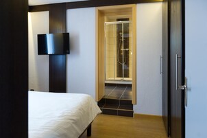 Una habitación de hotel moderna con una cama, un televisor montado en la pared y una zona de ducha con puertas de cristal.