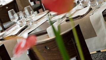 Una mesa de comedor dispuesta con varios vasos, cubiertos y un florero con una flor.