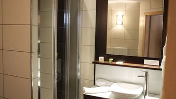 A modern bathroom with a glass shower enclosure, a sink with a mirror above, and two towels hanging on the wall.