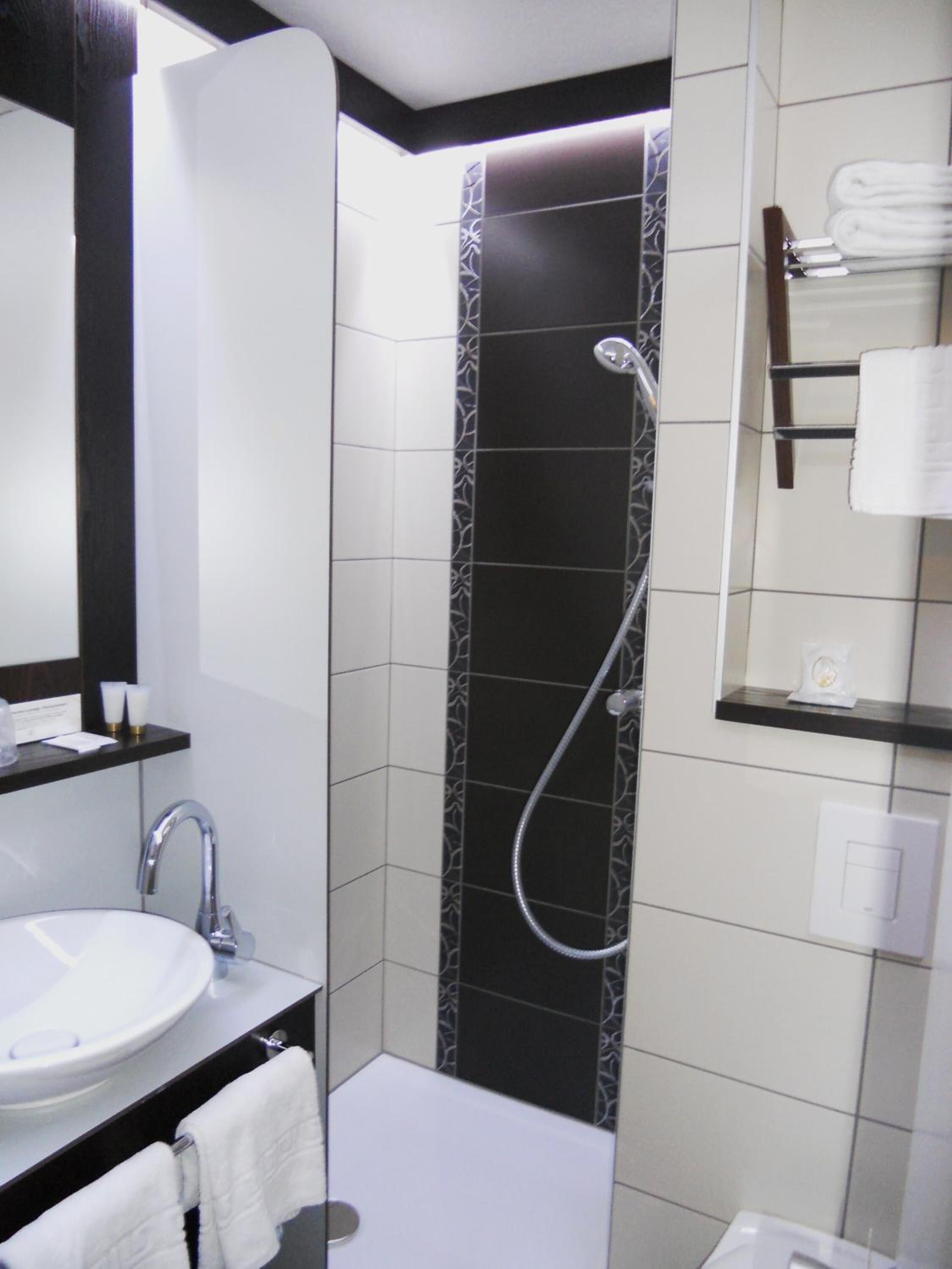 A modern bathroom with a white sink, a mirror, a shower with a handheld showerhead, and a towel rack.