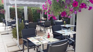 Un patio al aire libre con mesas y sillas, algunas con plantas en macetas.