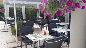 Un patio al aire libre con mesas y sillas, algunas con plantas en macetas.