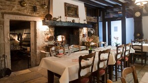 A rustic dining area with stone walls, a fireplace, wooden furniture, and a view of the street outside. - Auberge Le Renard'eau (Beze)