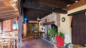 A rustic interior with wooden beams, a brick floor, and a stone fireplace. Tables and chairs are arranged for dining. - Auberge Le Renard'eau (Beze)