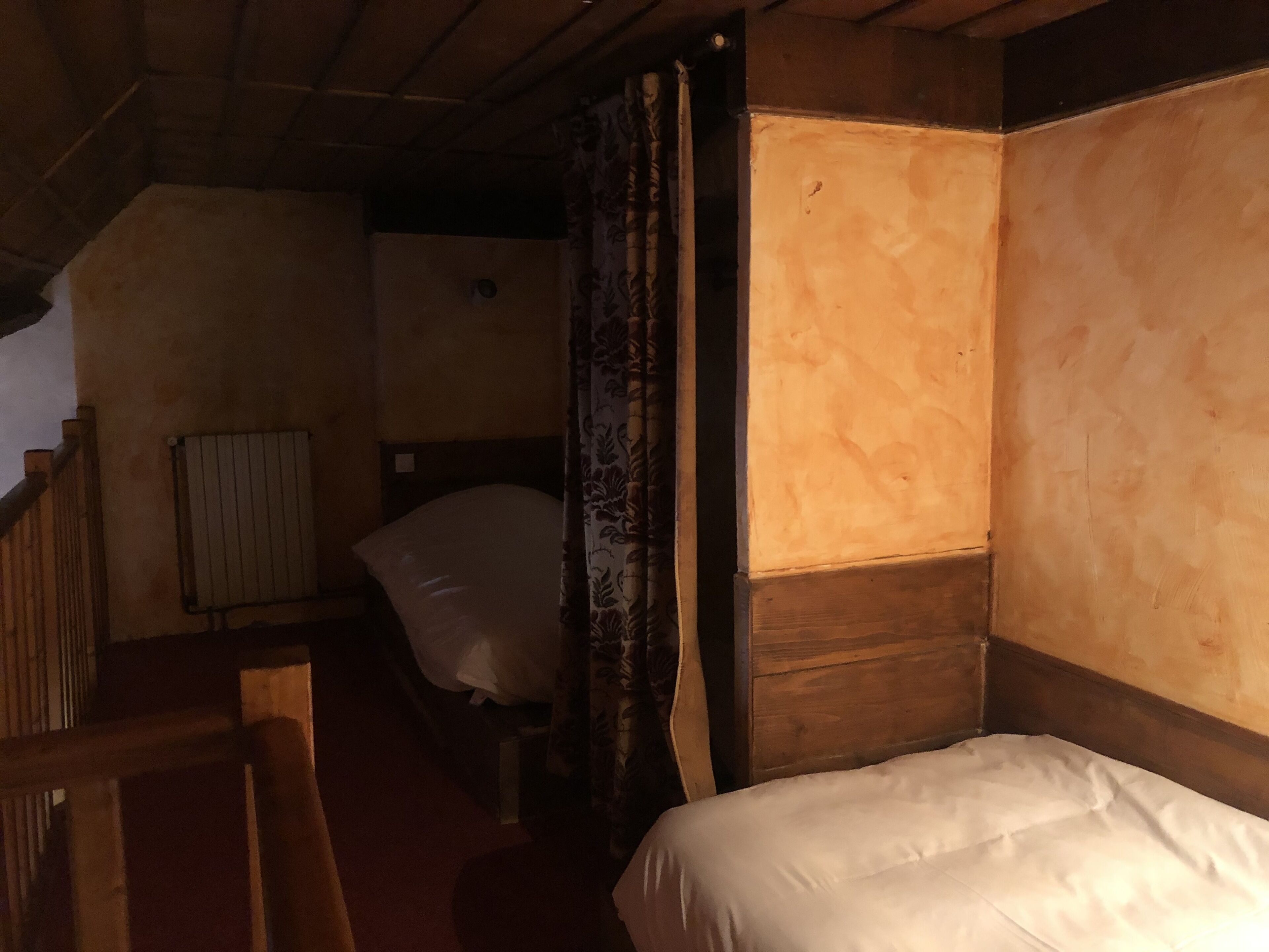 A narrow, dimly lit room with a single bed, a wooden headboard, and a radiator.