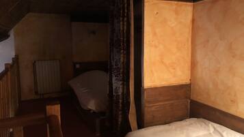 A narrow, dimly lit room with a single bed, a wooden headboard, and a radiator.